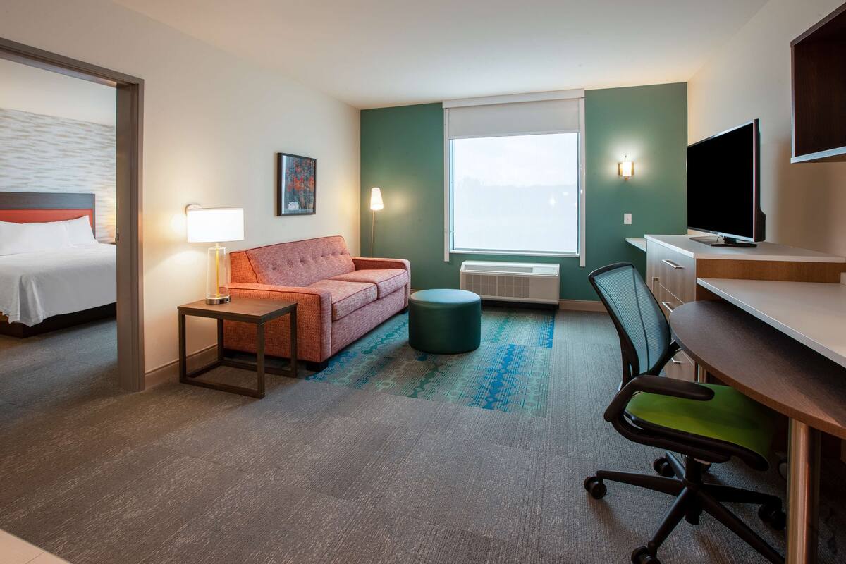Habitación de hotel con cama, escritorio, silla, sofá, lámpara, aire acondicionado y televisión.