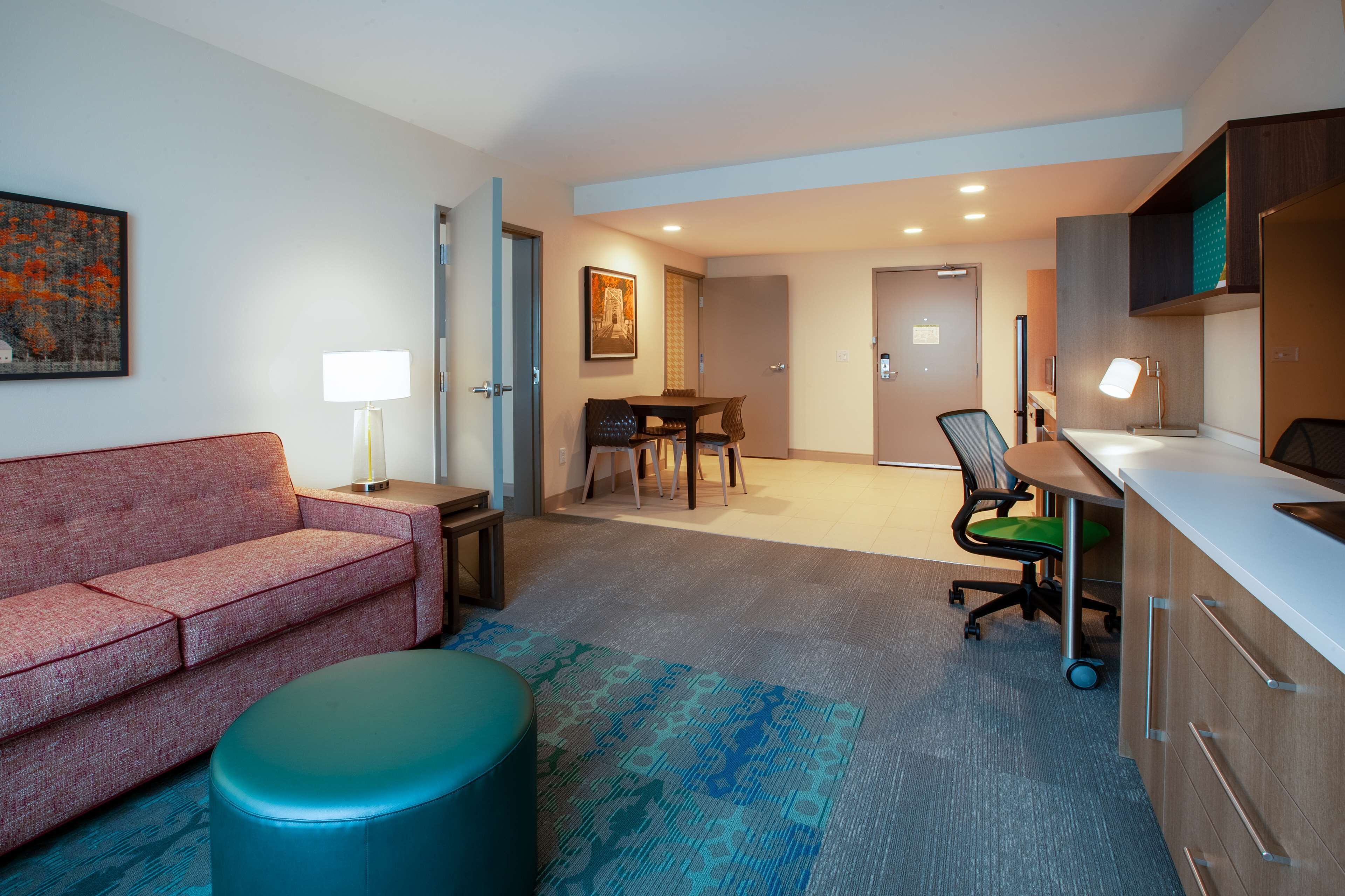 Una habitación de hotel moderna con sofá, una mesita, un escritorio con silla y una kitchenette.