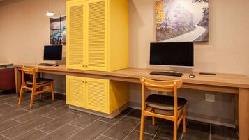 A workspace with two desks, each with a computer, keyboard, and mouse. There are two chairs, one on each desk. The room has a tiled floor and a large yellow cabinet.