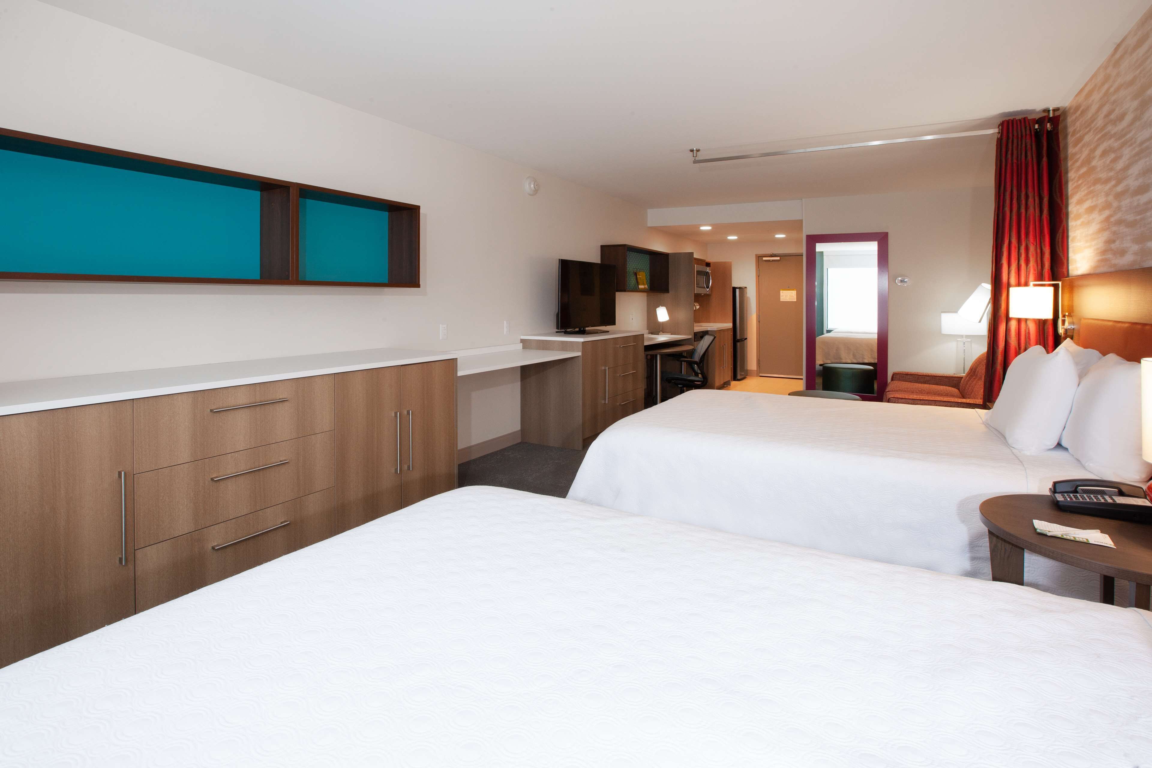 A hotel room with two beds, a kitchenette, a TV, and a bathroom visible through an open door.