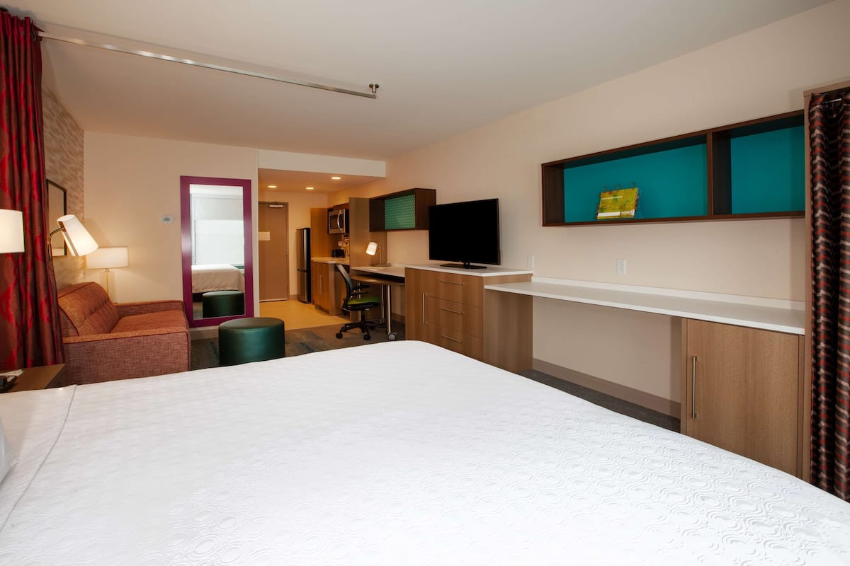 Habitación de hotel con una cama grande, un escritorio con computadora, televisor y un pequeño espacio de descanso.