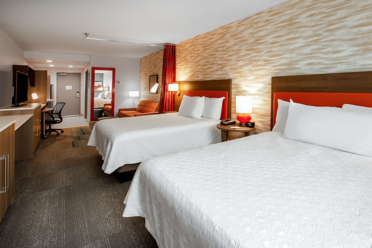 Habitación de hotel con dos camas, un escritorio, una silla y un televisor.