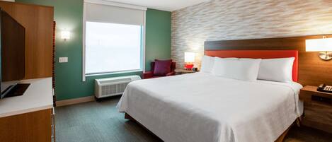 Habitación de hotel con una cama grande, un escritorio, una silla, un ventanal y una lámpara de pared.
