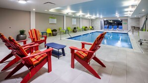 Ein Poolbereich mit roten und gelben Stühlen, einem blauen Tisch und einem Pool mit klarem, blauem Wasser.