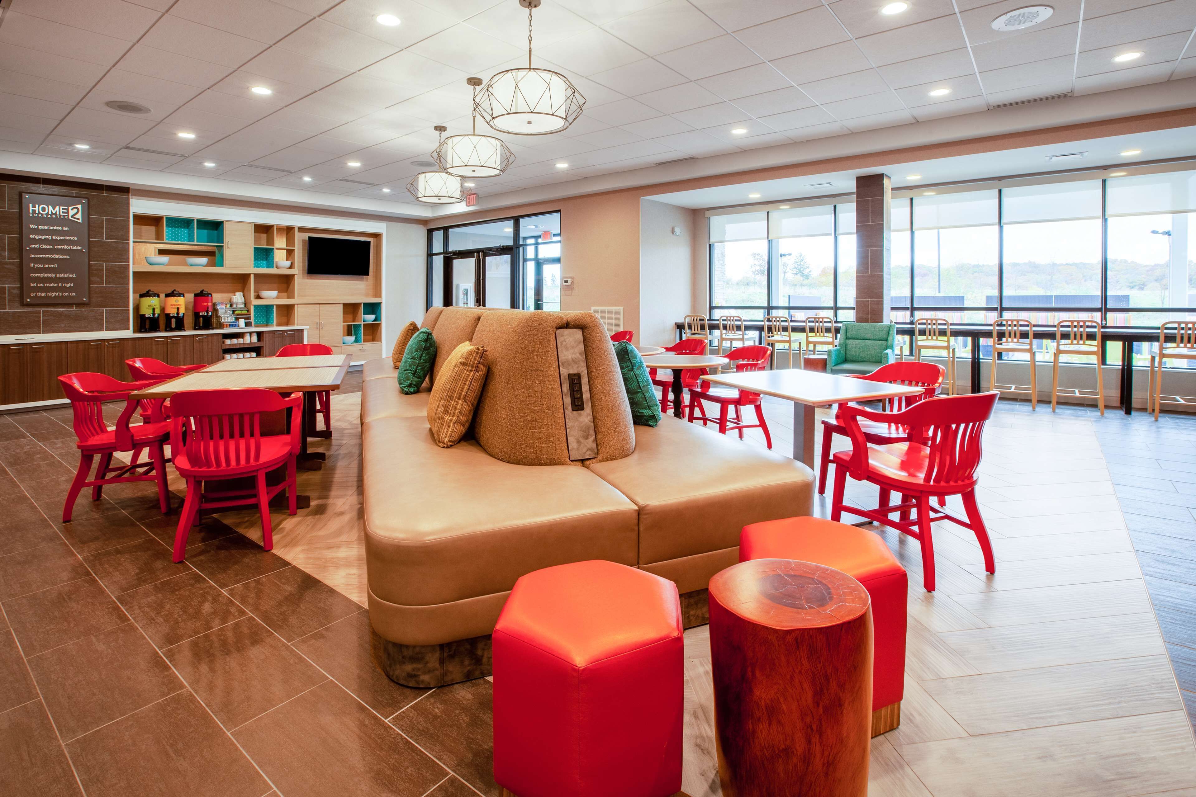 A modern dining area with red chairs, a beige sofa, and a large window offering a view.