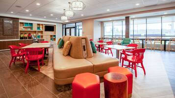 A modern dining area with red chairs, a beige sofa, and a large window offering a view.