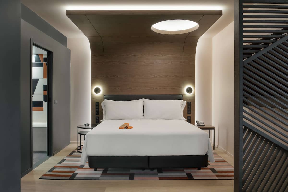A modern hotel room with a large bed, bedside tables, and a unique ceiling design.