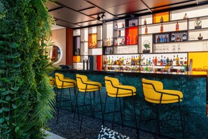 Eine Bar mit grüner Wand, gelben Barhocker und Regalen mit Flaschen und Gläsern.