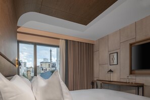 A hotel room with a bed, a desk, a TV, and a window with a view of buildings and a tower. - Canopy by Hilton Paris Eiffel Tower (Paris)