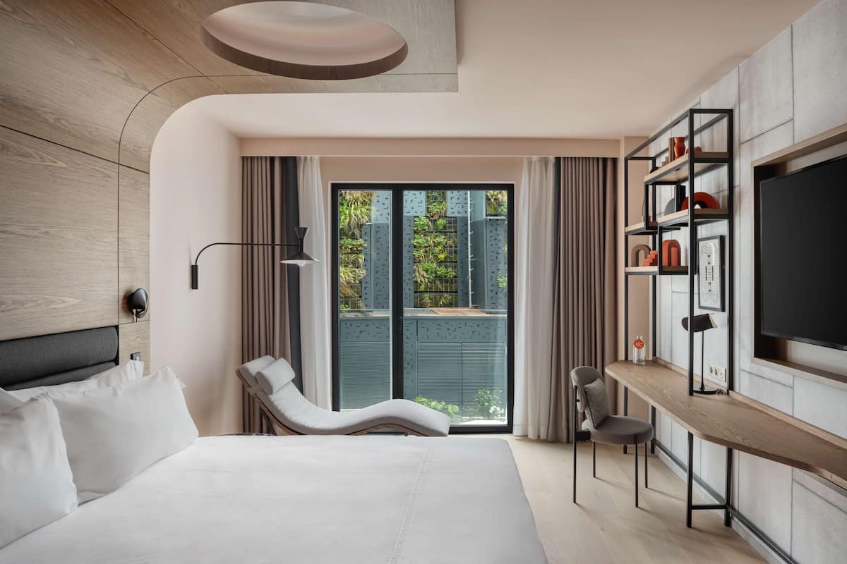 A modern hotel room with a large bed, a desk, and a TV.