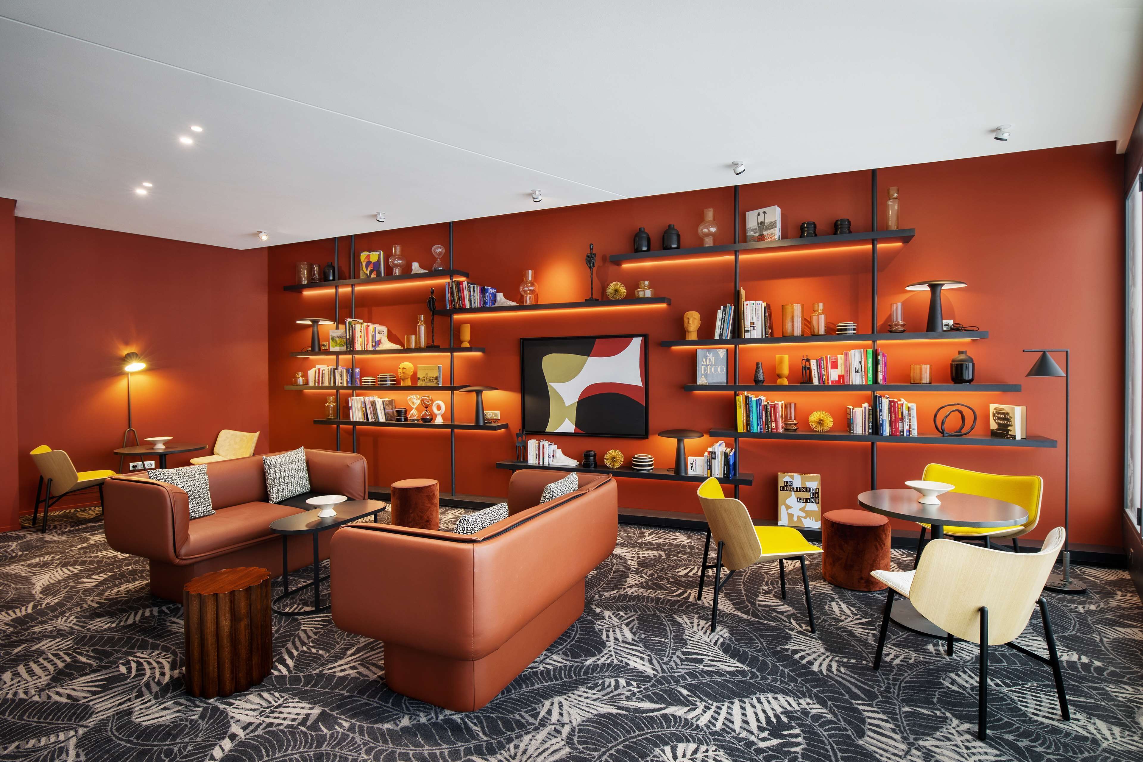 Un área de estar moderna con sofá, sillones, una mesita de centro y una estantería llena de libros y objetos decorativos.