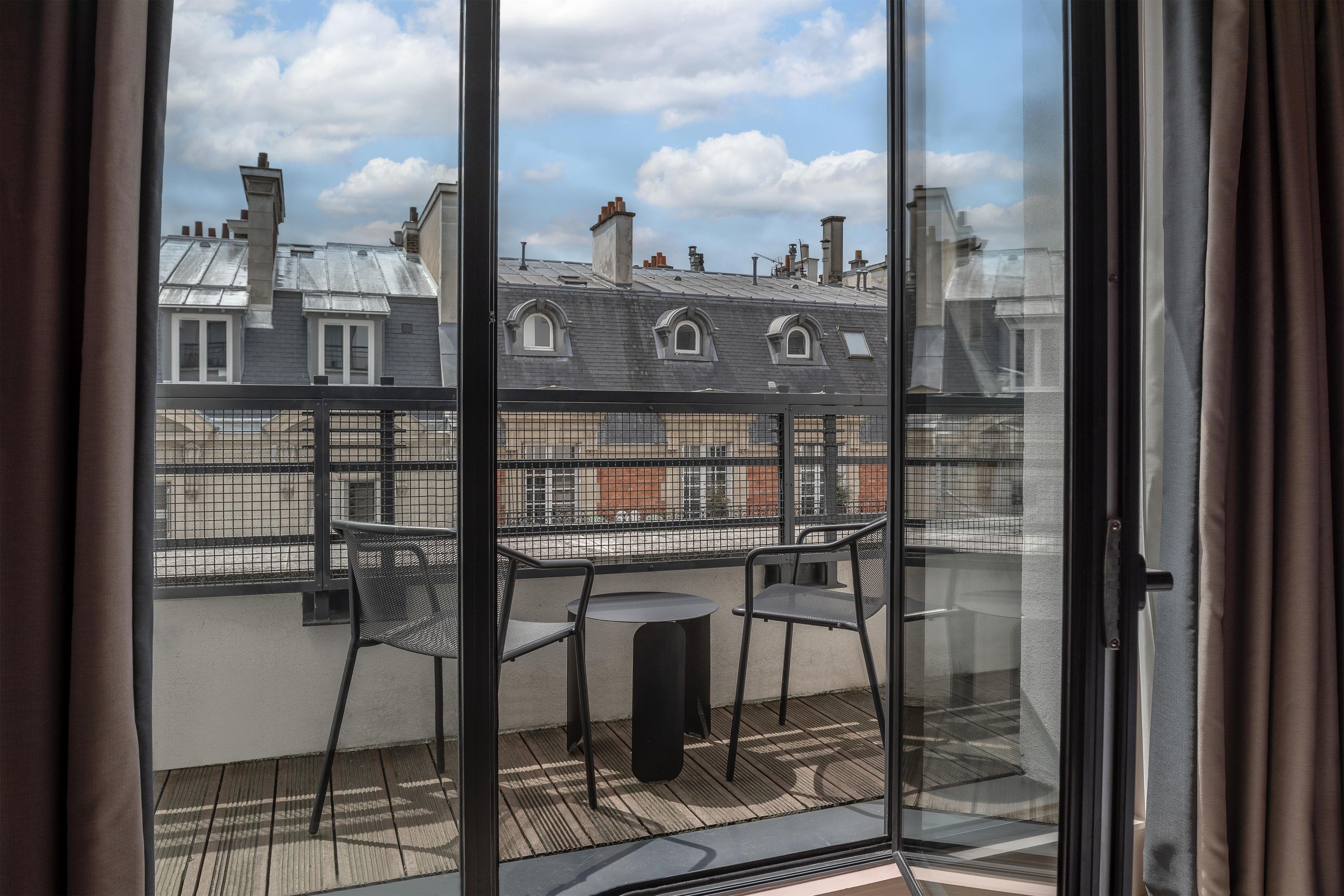 A balcony with a table and chairs, overlooking a residential area with multiple buildings.