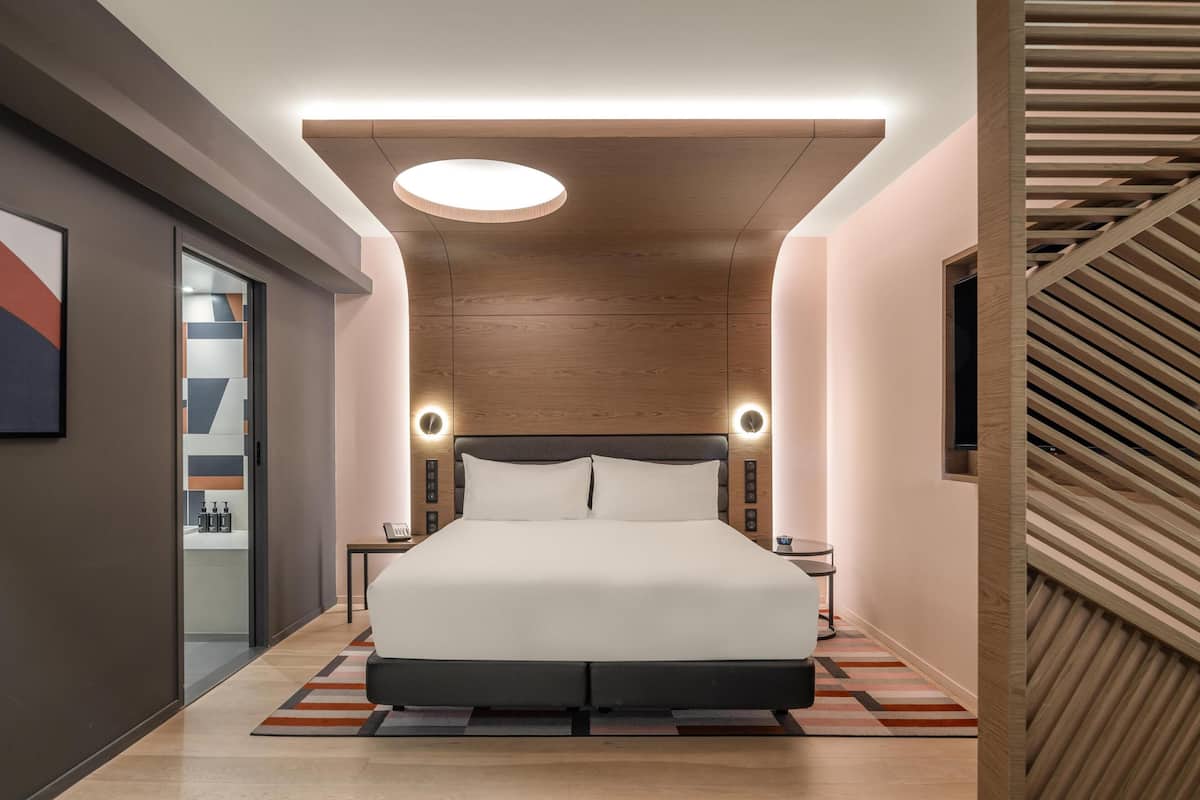 A modern hotel room with a large bed, a wooden ceiling, and a small bedside table with a lamp.