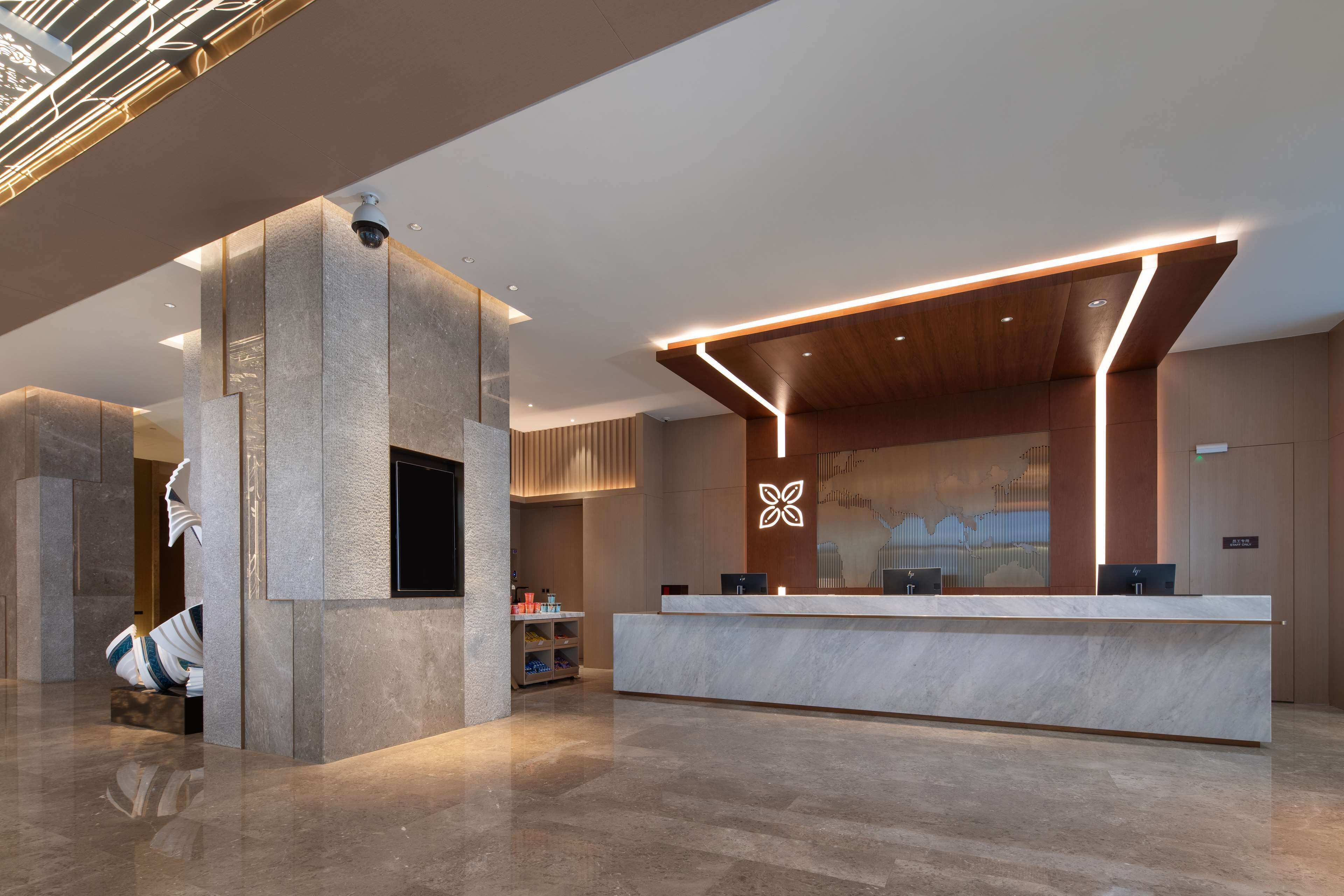 Una moderna zona de recepción con mostrador de mármol, pantalla digital y diseño de techo de madera.