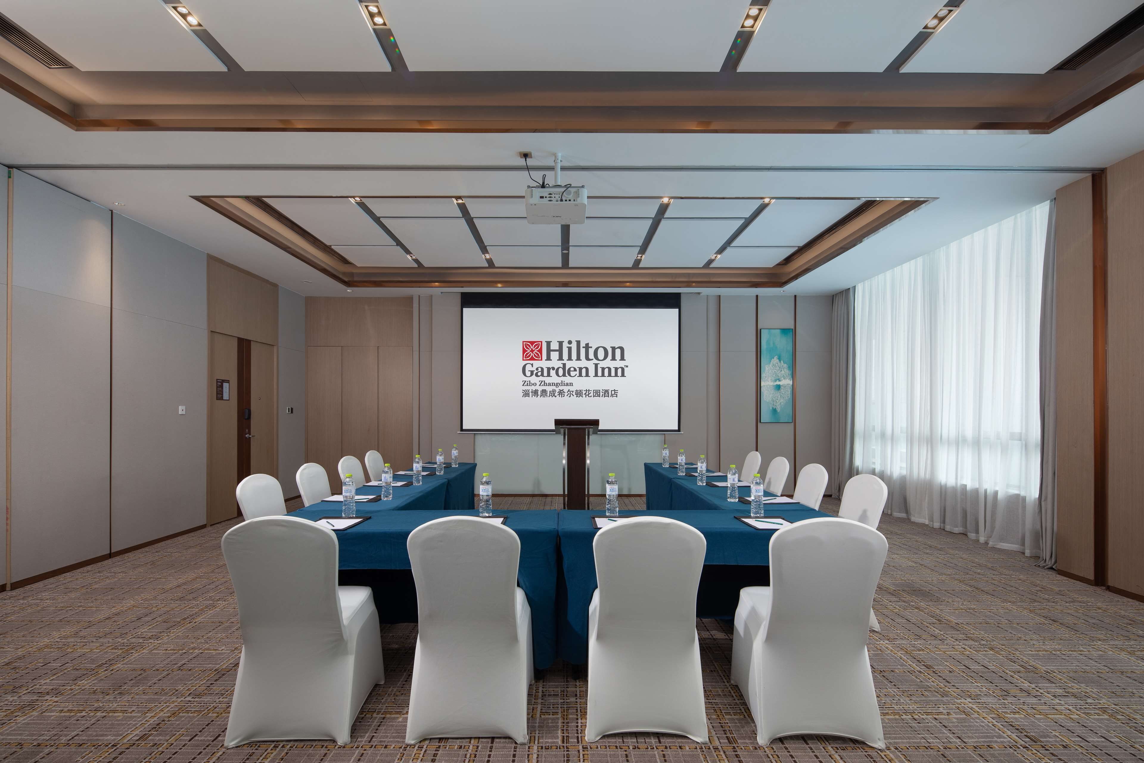 A conference room with a large screen displaying Hilton Garden Inn logo, a long table with chairs, and a projector.