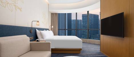 Una habitación de hotel moderna con una cama grande, un sofá, un televisor de pantalla plana y vistas a edificios altos.