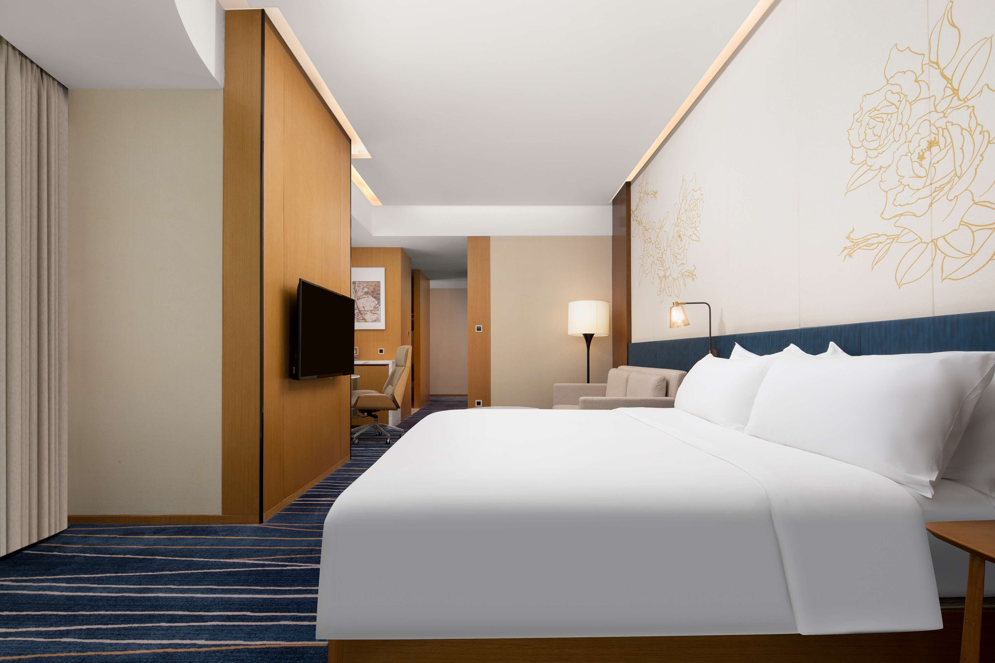 A hotel room with a large bed, a desk with a chair, a TV, and a lamp.