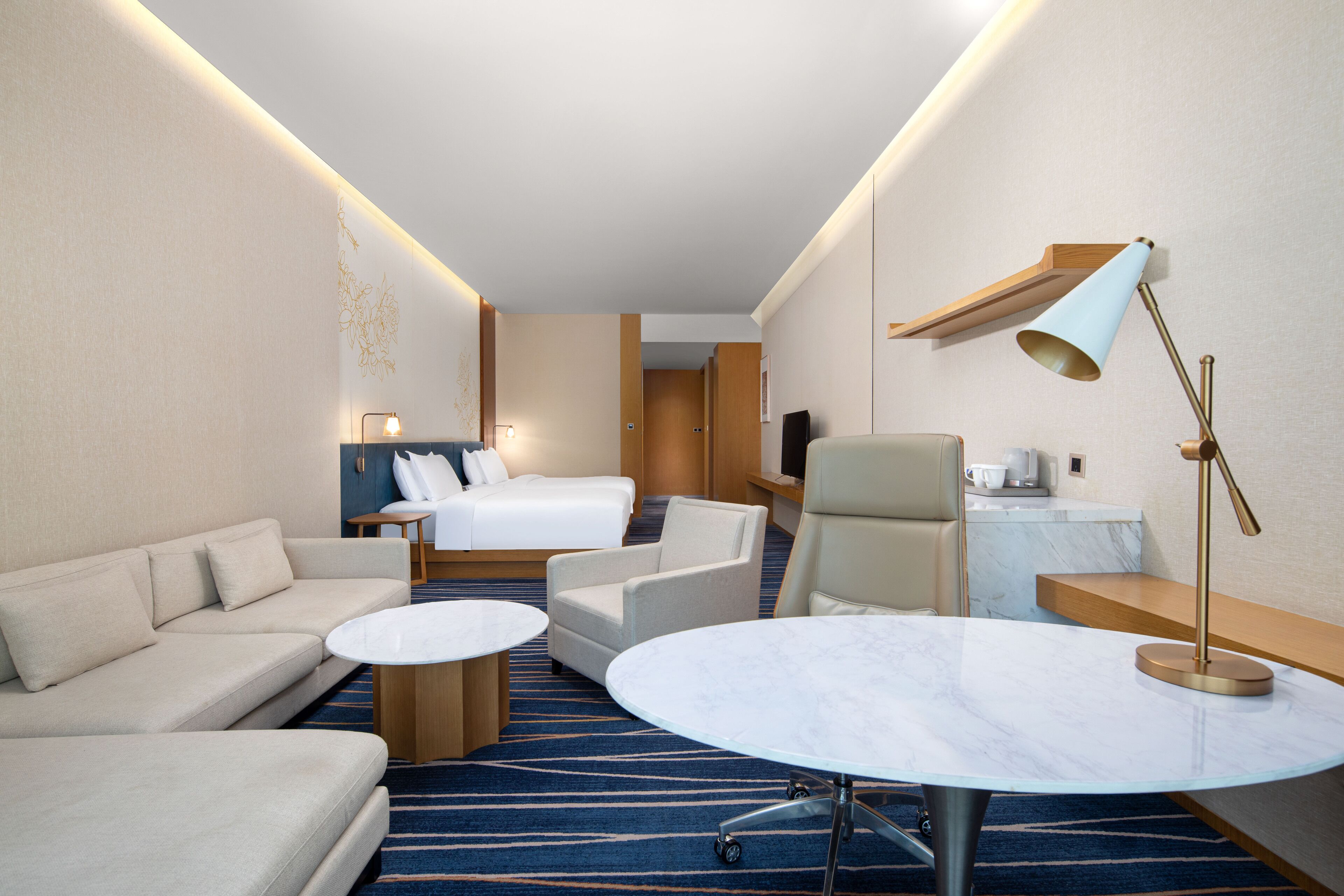 A hotel room with a sofa, a bed, a round table, a chair, and a desk with a lamp.