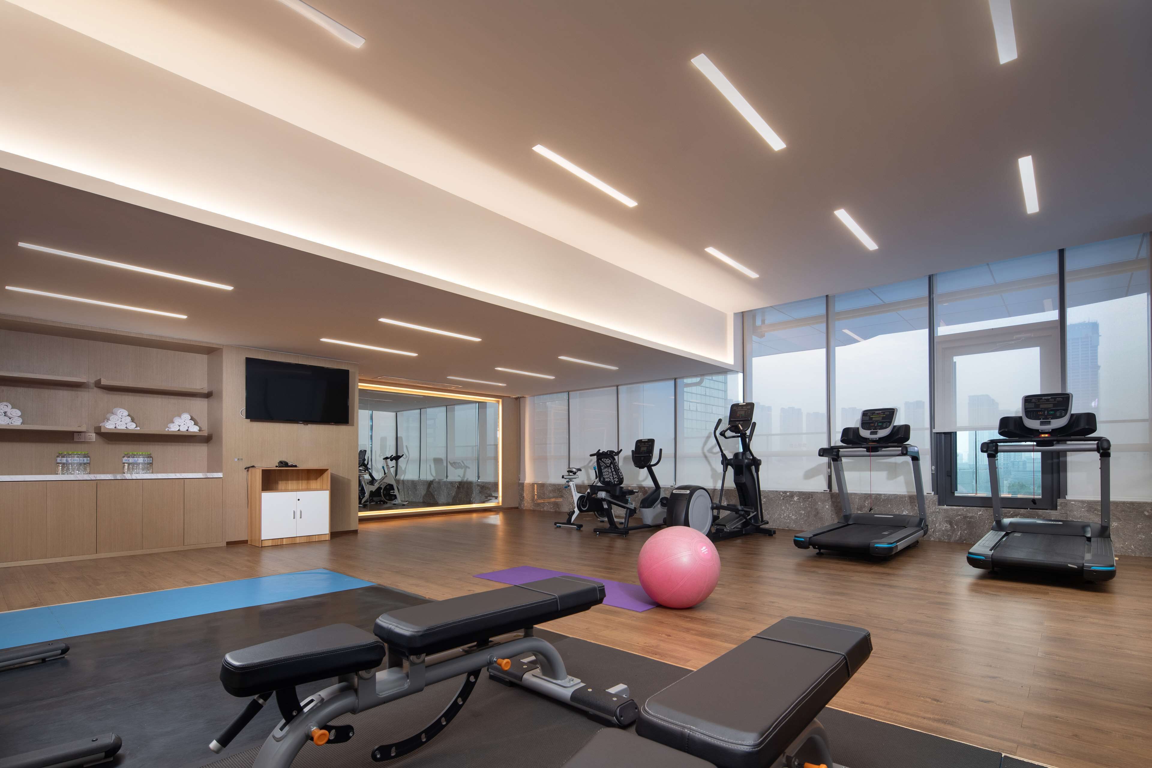 Ett modernt gym med träningsutrustning, en stor spegel och utsikt över staden genom stora fönster.