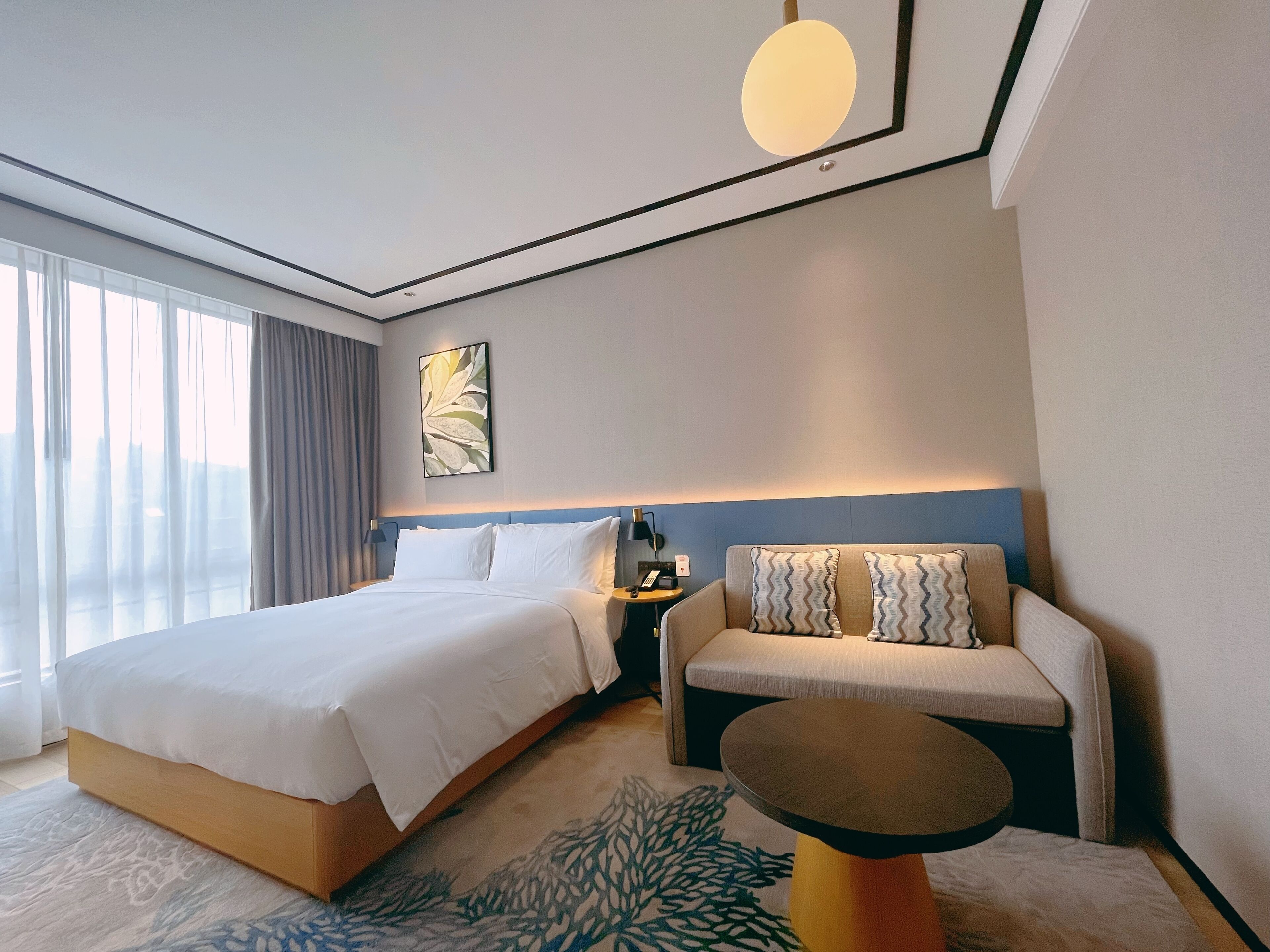 Una habitación de hotel con una cama grande, un sofá, una mesita y una lámpara fijada en la pared.