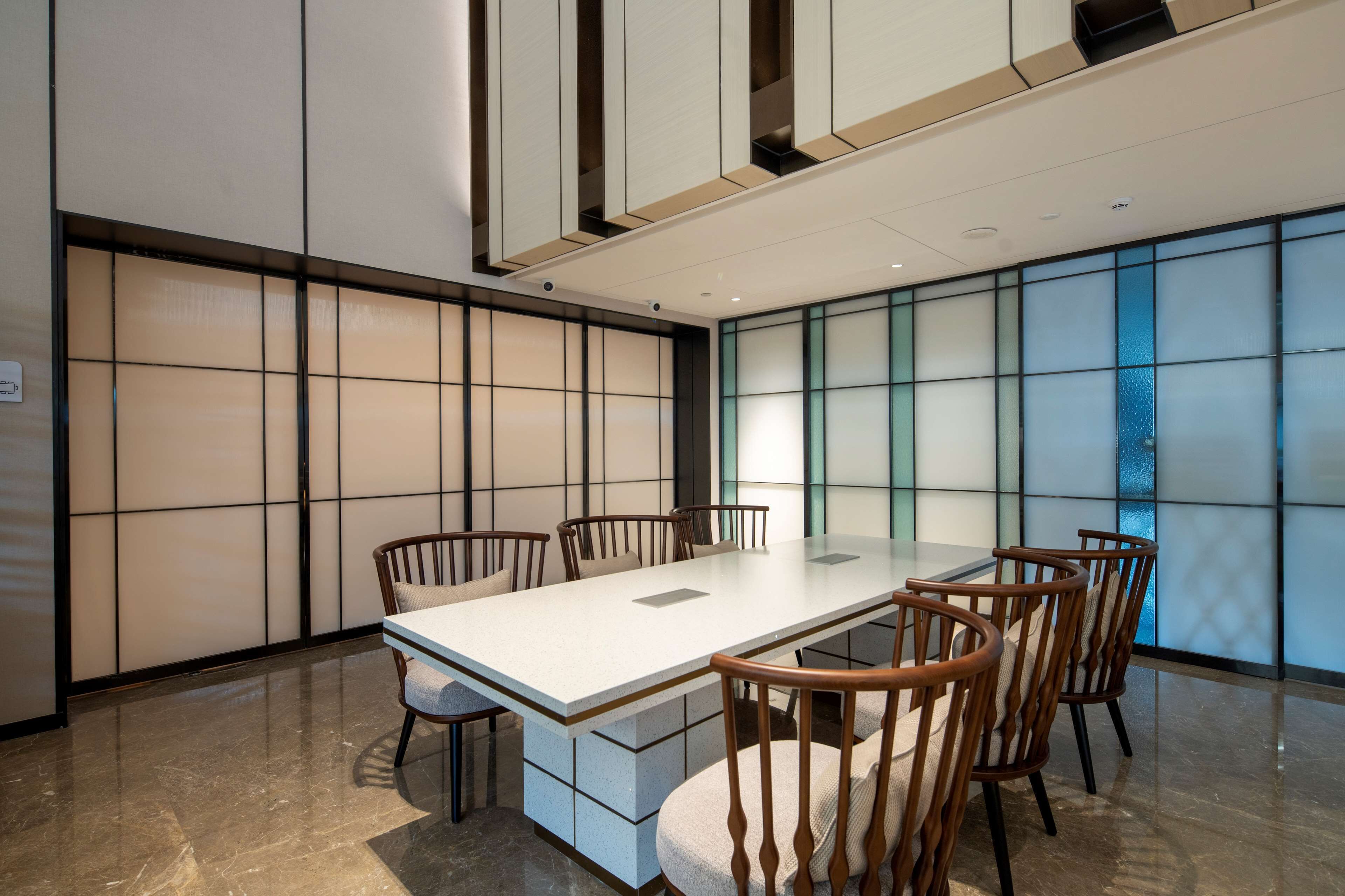 A modern meeting room with a long table and six chairs, large windows with frosted glass panels, and a polished marble floor.
