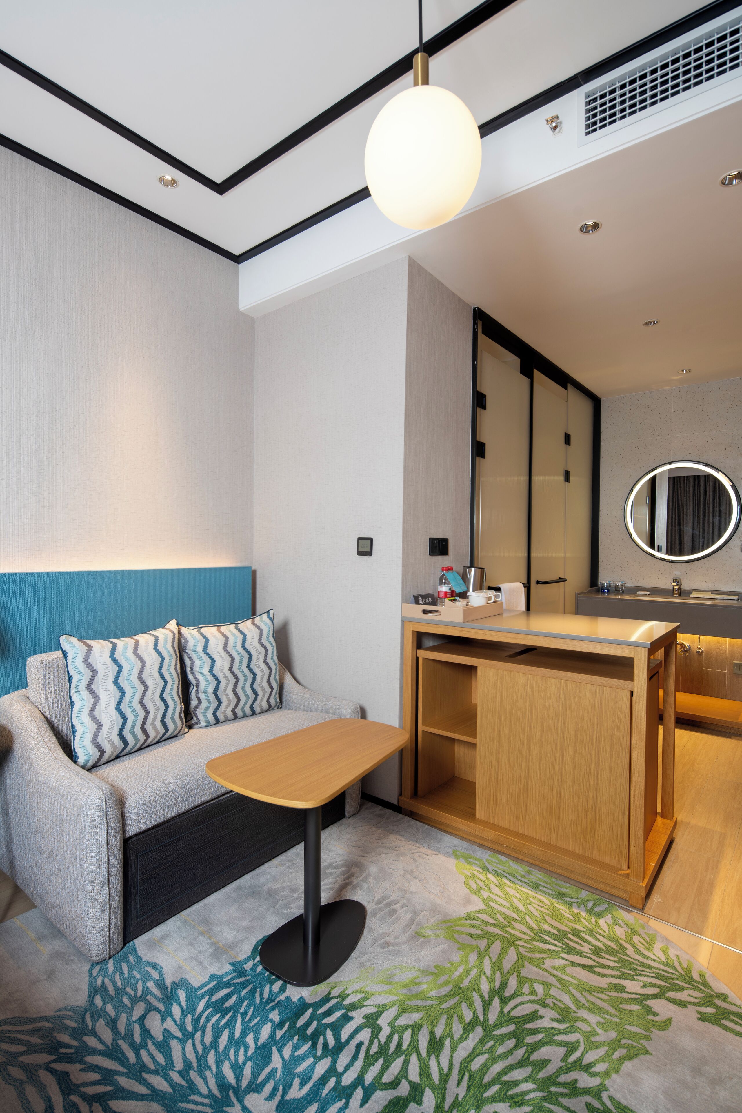 Quarto de hotel moderno com sofá, mesa pequena, armário de madeira e cozinha compacta.