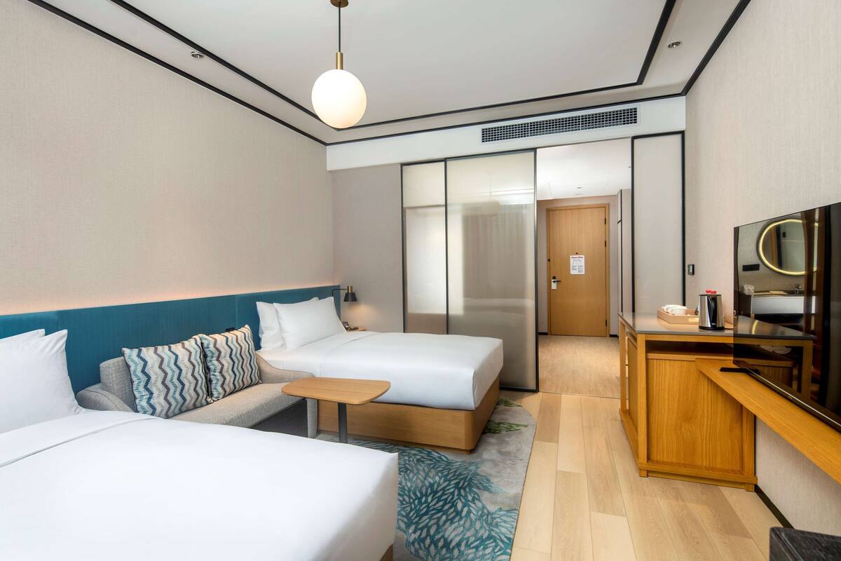 Ett hotellrum med två sängar, ett litet bord, en TV och ett litet kök.