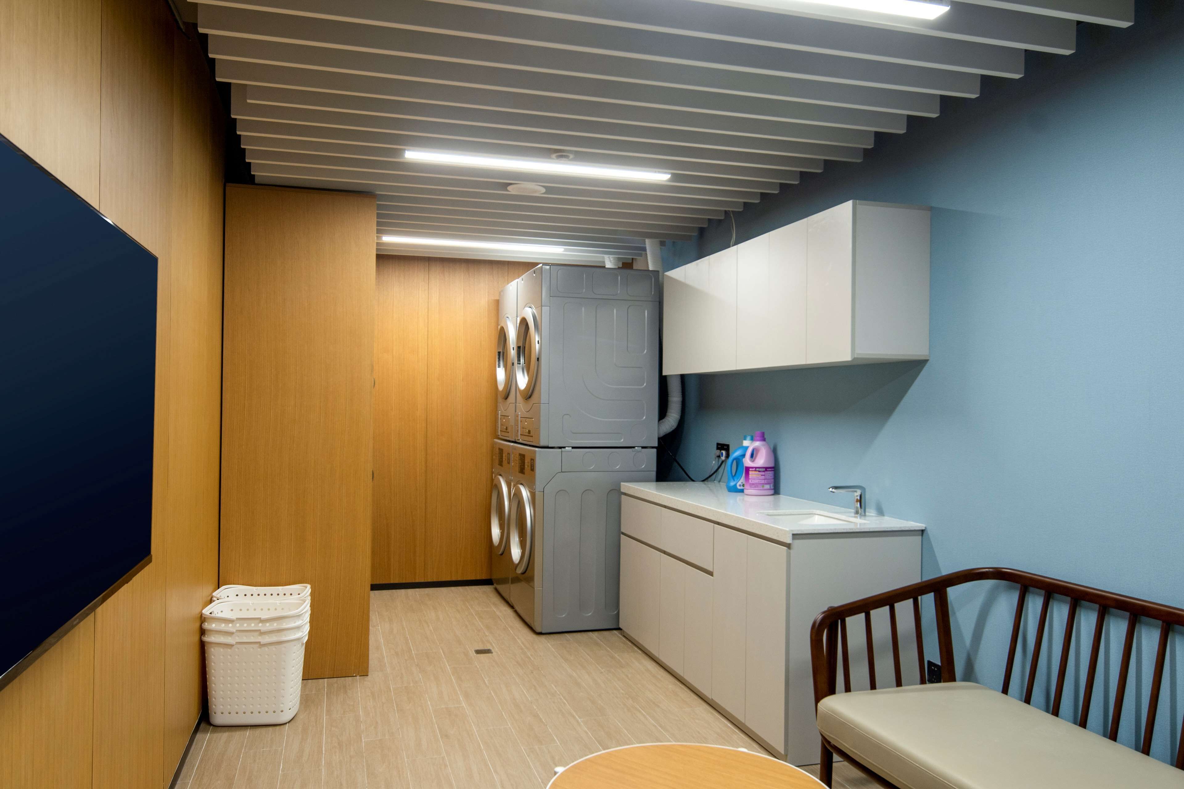 A compact kitchen with a washing machine, a sink, and a wooden chair.