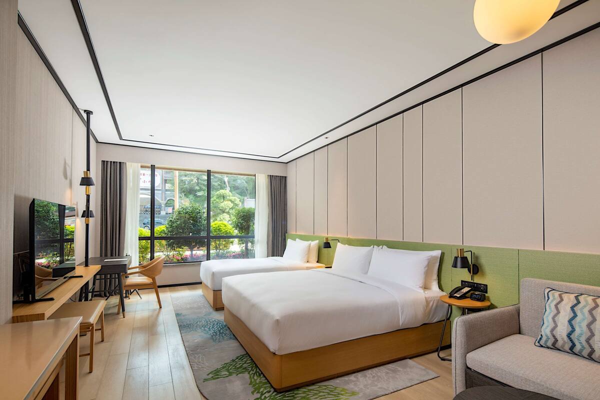 Ett modernt hotellrum med två sängar, ett skrivbord med en stol, en soffa och en TV.