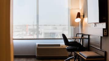 A modern office space with a large window, an air conditioning unit, a desk, a chair, and a wall-mounted TV.
