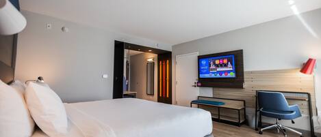 Une chambre d’hôtel moderne équipée d’un grand lit, d’un bureau, d’une chaise et d’un téléviseur à écran plat fixé au mur.