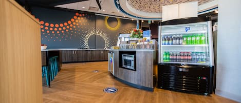 A modern kitchen area with a built-in refrigerator stocked with beverages, a microwave, and a coffee machine.
