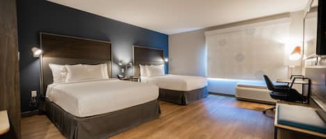 Habitación de hotel con dos camas, un escritorio, una silla y un ventanal grande con persianas.