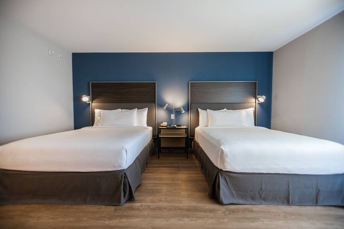 Een hotelkamer met twee eenpersoonsbedden, houten vloeren en een nachtkastje met een lamp ertussen.