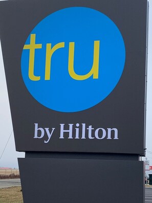 Une enseigne avec le logo « tru by Hilton » sur un fond sombre.