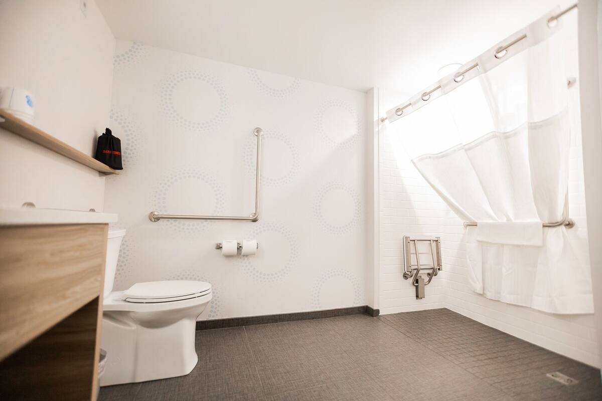 Een moderne badkamer met toilet, handgrepen, douchegordijn en handdoekhouder.