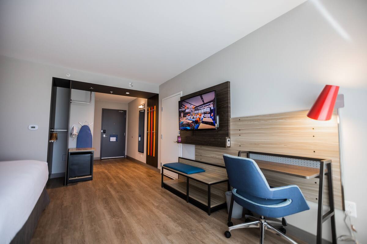 Een moderne hotelkamer met een bed, bureau, stoel, televisie en een rode lamp.