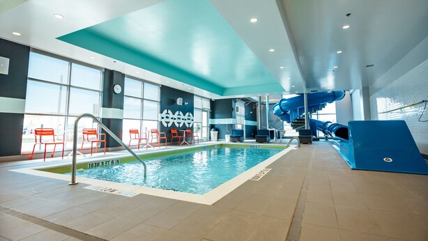 Una piscina interior con un tobogán azul, sillas rojas y un reloj en la pared.