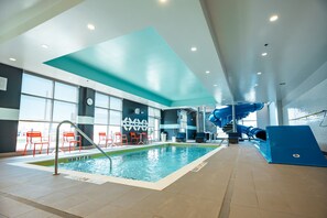 Una piscina interior con un tobogán azul, sillas rojas y un reloj en la pared.