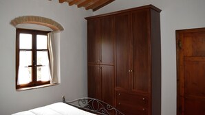 A bedroom with a bed, a wooden wardrobe, a window with curtains, and a wooden door.