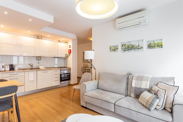 A modern kitchen with white cabinets, a dining area with a table and chairs, and a living room with a sofa and a lamp.