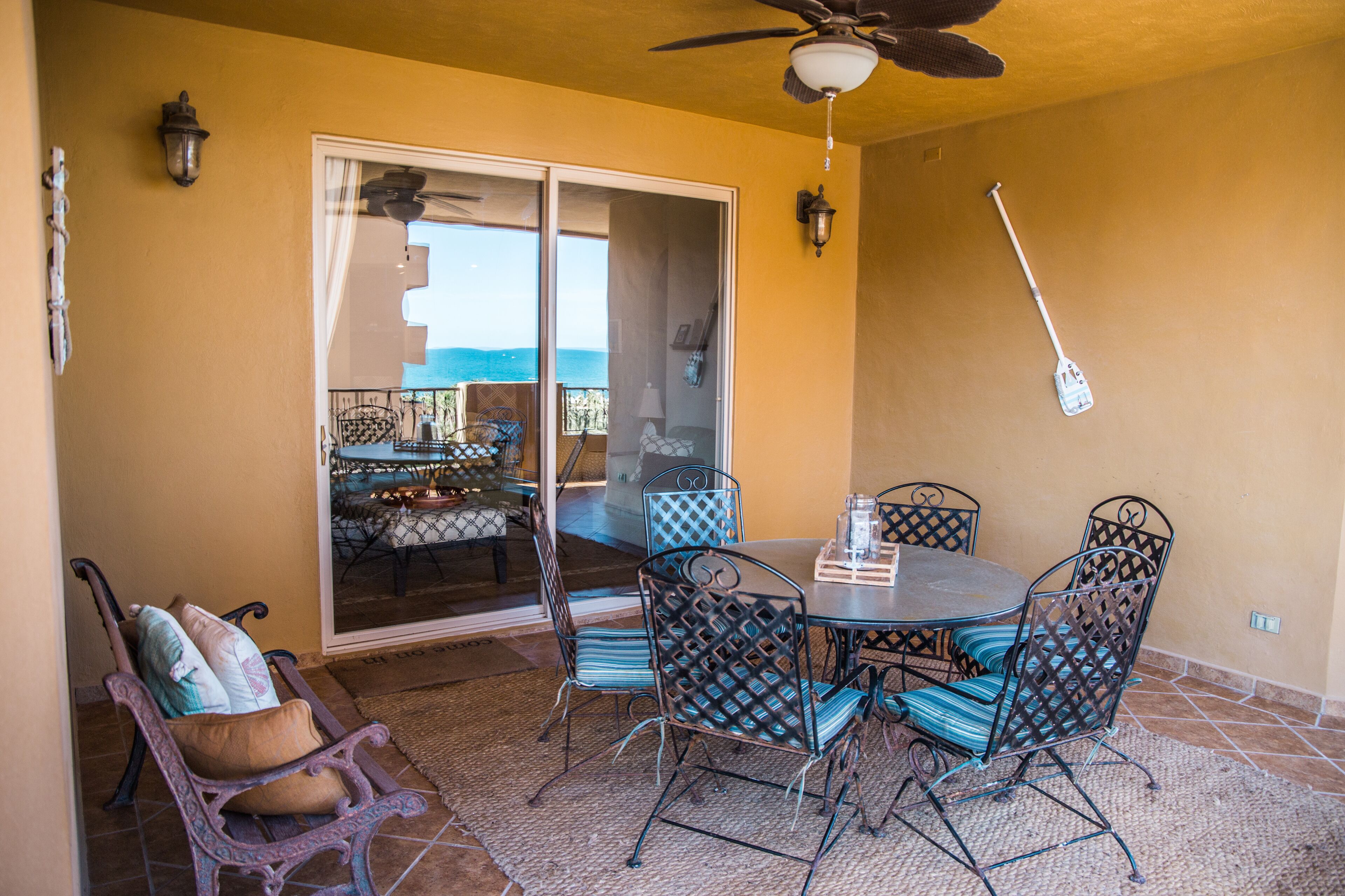 Une terrasse extérieure avec une table et des chaises, un ventilateur de plafond et une vue à travers une porte vitrée.