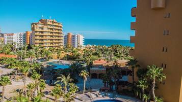 A resort with a swimming pool, palm trees, and a view of the ocean.