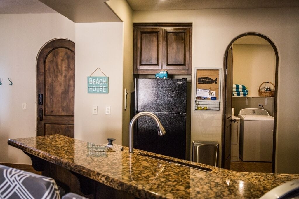 A kitchen with granite countertops, a black refrigerator, wooden cabinets, and a sign that says "Beach House".