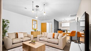 A modern living room with two sofas, a coffee table, and a dining area with orange chairs.