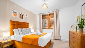 A modern hotel room with a large bed, a wooden nightstand, a dresser, and a window with curtains.