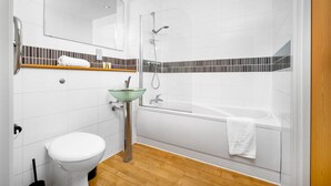A modern bathroom with a glass sink, a toilet, a shower, and a bathtub.