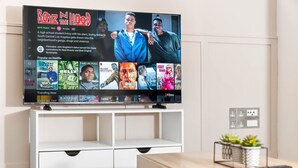 Een flatscreen televisie bevestigd aan een witte televisiemeubel met een afstandsbediening op een houten tafel ernaast.