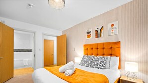 Een hotelkamer met een groot bed, een houten hoofdbord, een nachtkastje met een lamp en kunst aan de muur.