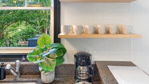 A modern kitchen with a granite countertop, a coffee maker, and a window with a view of greenery.